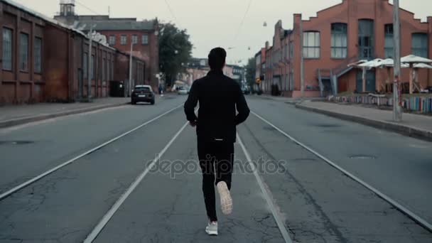 Αθλητής που τρέχει στη μέση του δρόμου. Βολή στο παρασκήνιο. Αργή κίνηση. Πίσω όψη μεταξύ των κομματιών του τραμ. — Αρχείο Βίντεο