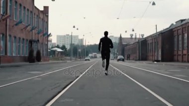Eski bir sokak ortasında hızlı koşan adam. Gerçek zamanlı vurdu. Özgürlük. Kamera sporcu arasında tramvay izlerini takip ediyor.