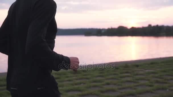 Slow motion. Sportsman enjoying healthy lifestyle. Young free male athlete running at peaceful sunset lake. Side view. — Stock Video