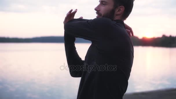 Cámara lenta cerca del hombre estirando los brazos en el lago. Vista frontal del feliz calentamiento masculino inteligente en la hermosa mañana tranquila . — Vídeos de Stock