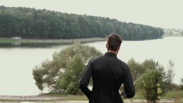 Zpomalený pohyb. Muž běh z kopce na břehu jezera. Kamera sleduje mladý muž jde dolů strmé kopce. Zpět na pozadí — Stock video
