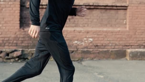 Vista lateral del hombre empezando a correr. En cámara lenta. Corredor masculino haciendo ejercicio en ropa deportiva negra. Seguimiento de disparo de cerca . — Vídeo de stock