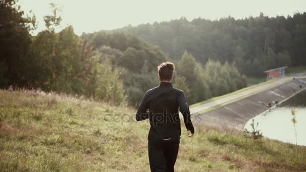 Zeitlupe. Mann rennt Grashügel hinunter Kamera begleitet Läufer beim Genießen der stimmungsvollen Herbstnatur. — Stockvideo