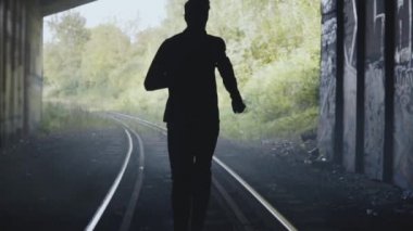 Ağır çekim adam siluet tren rayları üzerinde çalışan. Arkadan Görünüm. Arka plan atış biten. Özgürlük için takip.