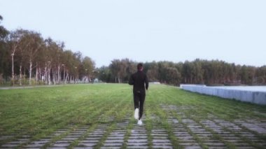 Ağır çekim. Sporcu zevk sağlıklı yaşam tarzı. Arka plan vurdu. Çim döşeme üzerinde koşan genç adam. Geri uzak görünümü.