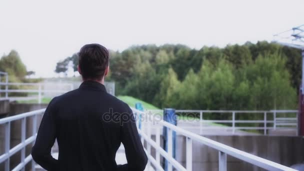 Ralenti vue arrière athlète appréciant le jogging. Jeune entraîneur de fitness qui court sur le pont du barrage vers un paysage rural calme . — Video