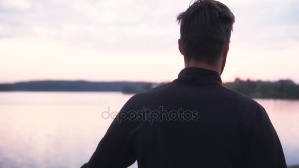 Hombre de cámara lenta estirando las piernas cerca de un lago tranquilo. Atrás vista atleta masculino preparándose para correr en el hermoso campo . — Vídeo de stock