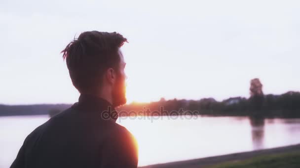 Atleta de câmera lenta correndo ao longo do lago nascer do sol. Homem de manga comprida preta a pensar na liberdade. Vista lateral . — Vídeo de Stock