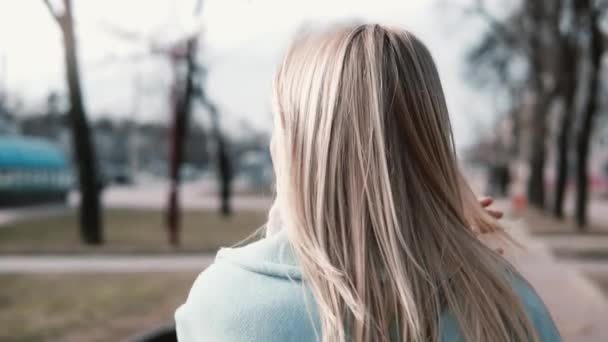 慢动作的女人在散步时整理头发。年轻的白种白人金发20s 蓝色温暖的大衣和围巾替身拍摄. — 图库视频影像