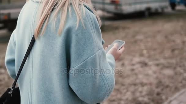 Mulher loira em câmera lenta usando redes sociais. Vista traseira. Menina sites de surf andando rua outono. Tiro de estilo de vida . — Vídeo de Stock