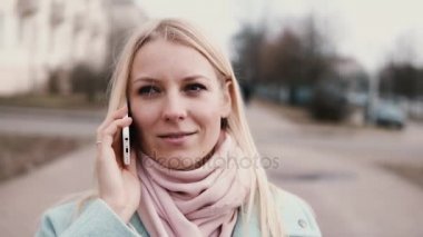 Ağır çekim beyaz bir kadın telefonla konuşuyor. Mutlu bir şekilde gülümseyen sohbet güzel şık güzel genç 20s sarışın.