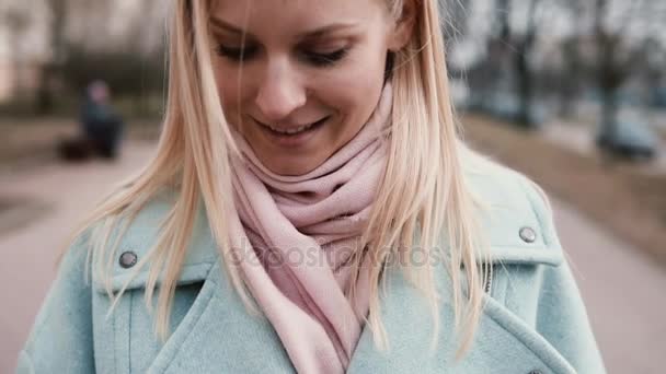 Slow motion gelukkig Kaukasische vrouw texting glimlachen. Mooie stijlvolle jonge 20s blonde messaging tijdens het wandelen. Close-up. — Stockvideo