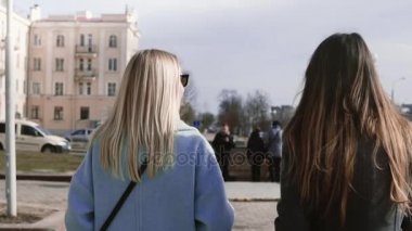 Yavaş hareket iki kızla beraber sokakta yürüyelim. Genç bayanlar güzel uzun saçlı şık giysiler içinde. Arkadan Görünüm.