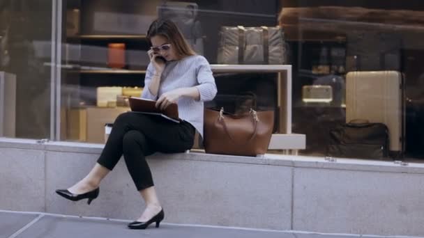 Joven mujer de negocios ocupada sentada cerca del escaparate, hablando por teléfono móvil y mirando en el calendario, cepilladora . — Vídeo de stock