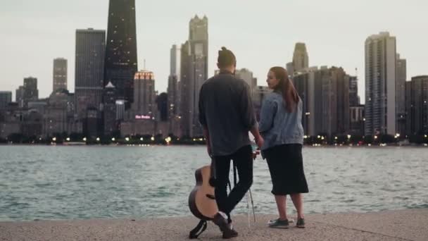 Unga kreativa par på stranden av Michigan laken, Chicago, Amerika. Kvinna som teckning, man håller gitarren i kväll — Stockvideo