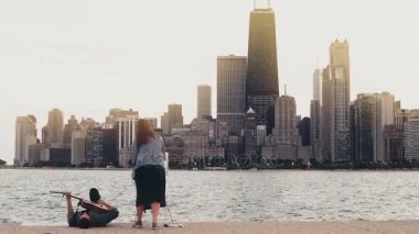 Genç yaratıcı Michigan Gölü kıyısındaki üzerinde Chicago, Amerika çift. Kadın çizmek, kıyıda yatan anne oyun gitar.