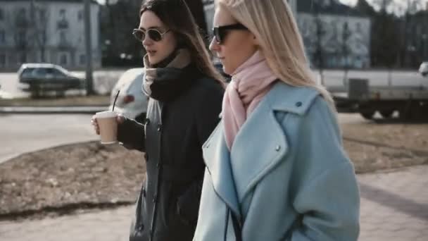 Två kaukasiska flickvänner promenader och chatta. Damer i snygga kappor skvaller i gatan. Kvinnor njuta av limning tid. — Stockvideo