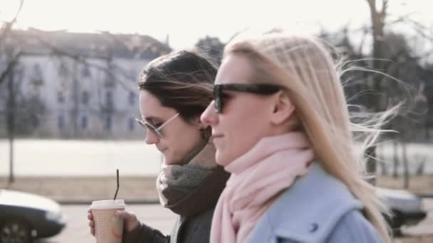 Slow motion blanke meisjes lopen chatten. Mooie dames in stijlvolle warme jassen en zonnebrillen praten in de straat. — Stockvideo