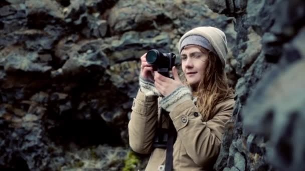 Jovem mulher bonita segurando câmera e tirando fotos nas montanhas. Viajando filmagem feminina sobre a natureza . — Vídeo de Stock