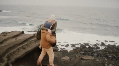 Arkadan görünüşü genç adam ve deniz kıyısında soğuk günde ayakta, el ele tutuşarak ve su almak üzerinde kadın.