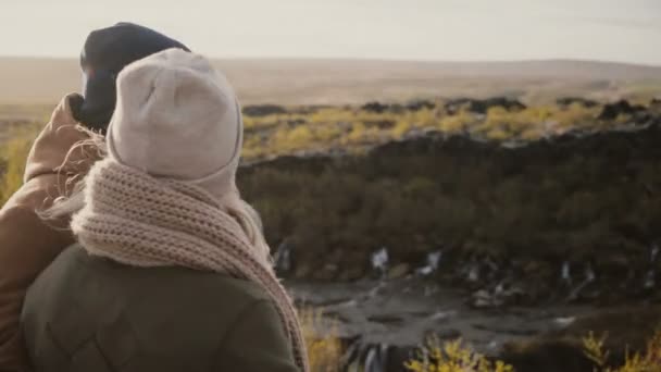 Rückansicht eines jungen Mannes und einer jungen Frau, die im sonnigen Tal stehen und die schöne Aussicht in Island genießen. — Stockvideo