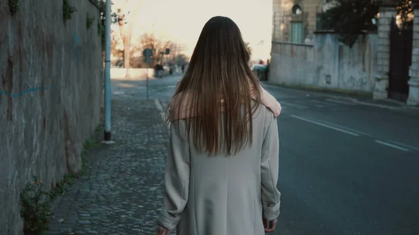 Back view of young lady walking in the city centre alone. Female with long hair going near the road, enjoying the day. — Stock Photo, Image