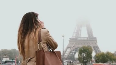 Paris, Fransa'nın şehir merkezinde yürüyüş ve cep telefonu üzerinde konuşurken genç mutlu bir kadın. Eiffel tower yakınındaki gülümseyen kadın