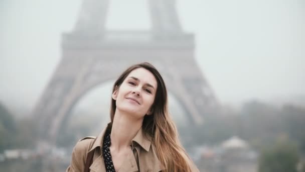 Retrato de uma jovem bela mulher em pé perto da Torre Eiffel, em Paris, França, olhando para a câmera e sorrindo . — Vídeo de Stock