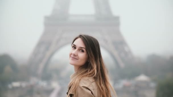 Joven mujer hermosa de pie cerca de la torre Eiffel en París, Francia, girando y mirando a la cámara y sonriendo . — Vídeos de Stock