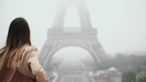 Vista trasera de la joven mujer elegante caminando en el centro cerca de la torre Eiffel en París, Francia en la mañana brumosa . — Vídeo de stock