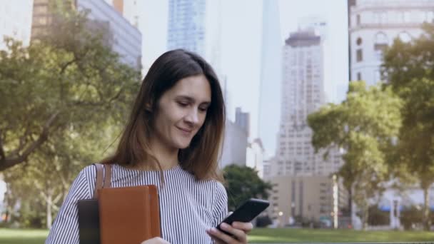 Joven mujer de negocios feliz de pie en el distrito financiero de Nueva York, EE.UU. y utilizando el teléfono inteligente como oficina móvil . — Vídeos de Stock