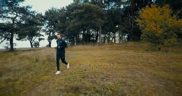 Läufer auf einem kleinen Pfad bergab. Drohne fliegt rückwärts, zoomt heraus und schwenkt großen gelben Hügel und Wald. — Stockvideo