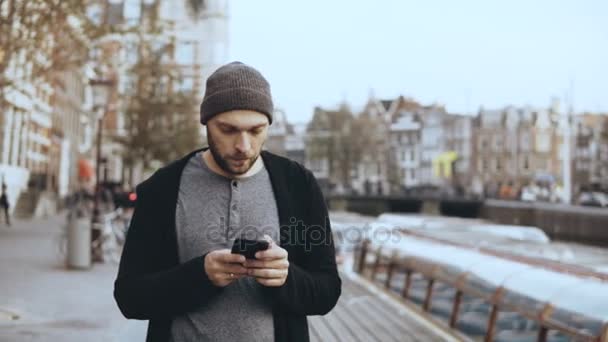 4k alkalmi koncentrált ember használ smartphone. Szép szakállas kreatív európai férfi a kalap textil-az utcán. — Stock videók