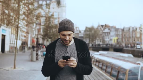 4k kaukasischen Touristen Mann zu Fuß mit Smartphone. lässige gutaussehende bärtige lächelnde erwachsene männliche SMS auf der Straße. — Stockvideo