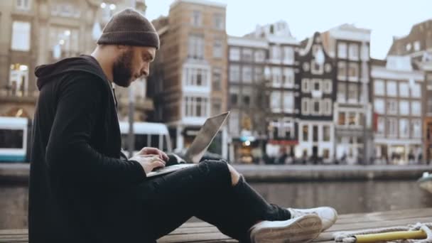 4K Jeune homme d'affaires créatif utilise ordinateur portable à l'extérieur. Homme prospère travaillant près d'un beau remblai de rivière, vieille ville . — Video