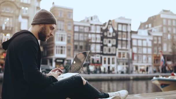 Молодой европеец из 4К работает с ноутбуком снаружи. Творческий работник ищет вдохновение в красивых пейзажах старого города . — стоковое видео