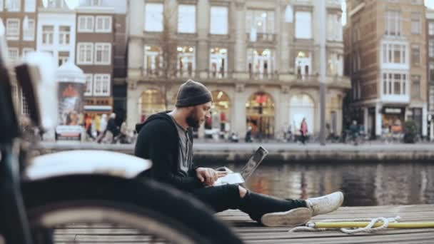 4K European man sitting with laptop in the street. Bicycle wheel in front of camera. Creative arts worker mobile office. — Stock Video