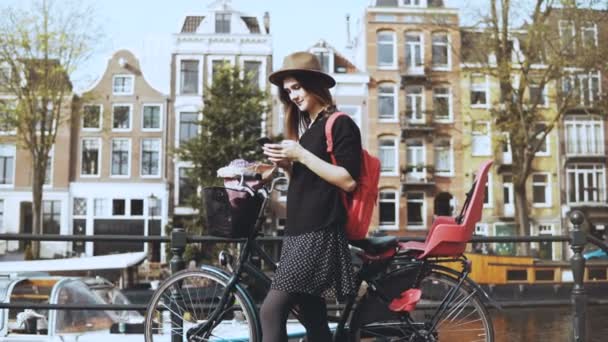 Blogger senhora com bicicleta em uma ponte da cidade velha. Feminino tipos turísticos europeus, olha em torno de desfrutar de dia ensolarado quente. 4K — Vídeo de Stock