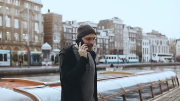Happy Caucasian man walks and talks on the phone. 4K. Excited creative tourist sharing emotions in Amsterdam old town. — Stock Video