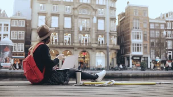 4K Young traveler woman in the street with laptop. European lady sitting in the street with red backpack and thermomug. — Stock Video