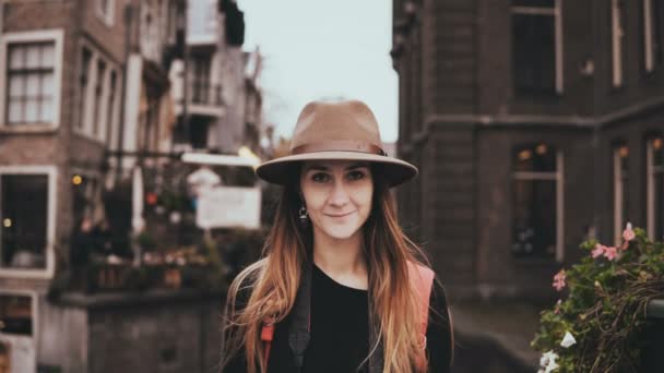 Portret van gelukkig Europees meisje camera kijken. Aantrekkelijke jonge dame in cool hoed met lange vliegende haar glimlachen. 4k. — Stockvideo