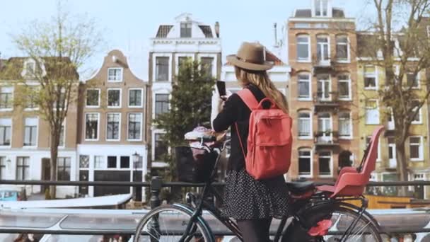 Tourist lady with bicycle takes photos on bridge. Cute Caucasian female photographs magnificent old town architecture 4K — Stock Video