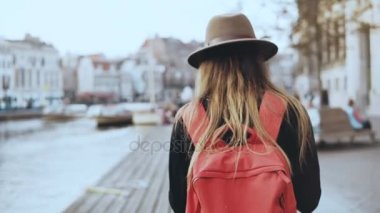 Kadın turist yürür, nehir iskele üzerinde fotoğraf çeker. Uzun saçlı kız, kırmızı sırt çantası online arkadaş resimler gönderir. 4k