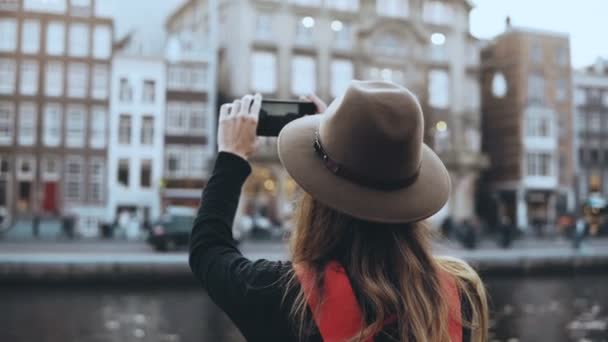 La señora del turismo toma fotos de la arquitectura antigua. Chica con el pelo largo y la mochila roja disfrutando de increíbles paisajes de la ciudad. 4K . — Vídeos de Stock
