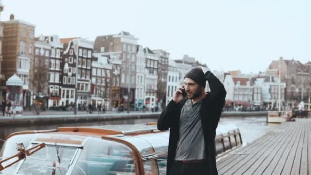 Happy European man walking, talking on the phone. 4K. Casual creative bearded businessman. River embankment in old town. — Stock Video