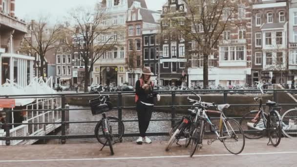 Mooie Kaukasische vrouw telefoon gesprek beëindigen. Straat fotograaf praat met haar vriend op rivier brug met fietsen. 4k — Stockvideo