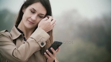 Sisli parkta genç güzel kadın portresi. Sabah smartphone kullanarak erkek gülümseyen.