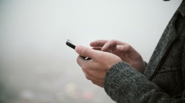 Erkek el cep telefonu dokunmatik ekran ile tutarak yakın çekim görünümü. Sisli parkta Smartphone kullanan genç adam.