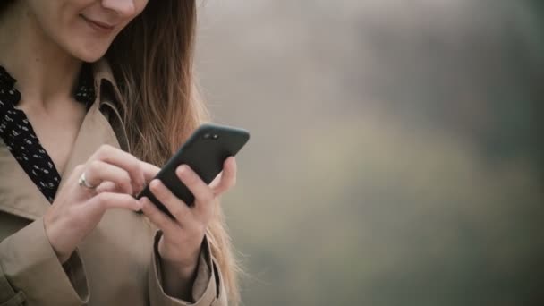 Close-up beeld van vrouwelijke handen met de mobiele telefoon met touchscreen. Jonge vrouw met behulp van smartphone in mistige park. — Stockvideo