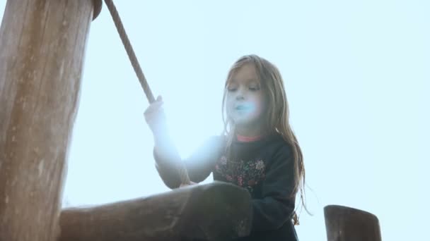 Porträt eines entzückenden kleinen Mädchens im Seilgarten. Glücklich lächelnde Mädchen gehen über Hindernisse auf dem Spielplatz. Schwenkschuss. — Stockvideo